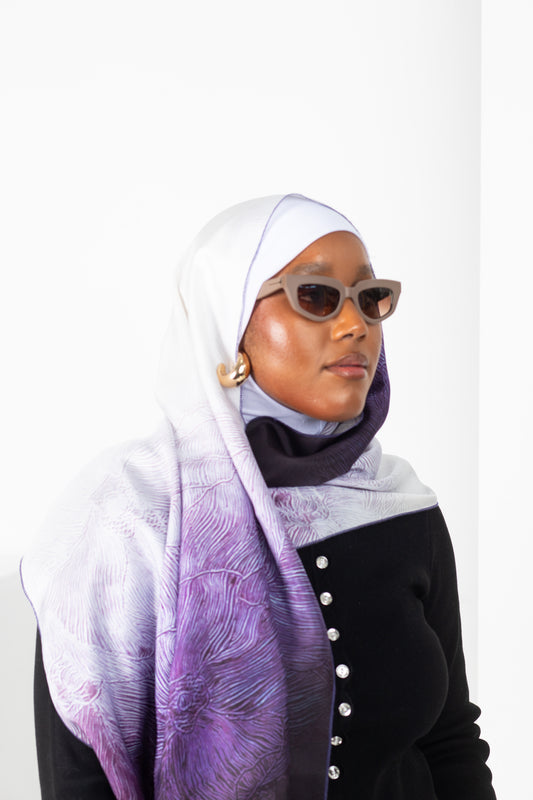 Woman wearing a white and purple patterned hijab with sunglasses on a white background